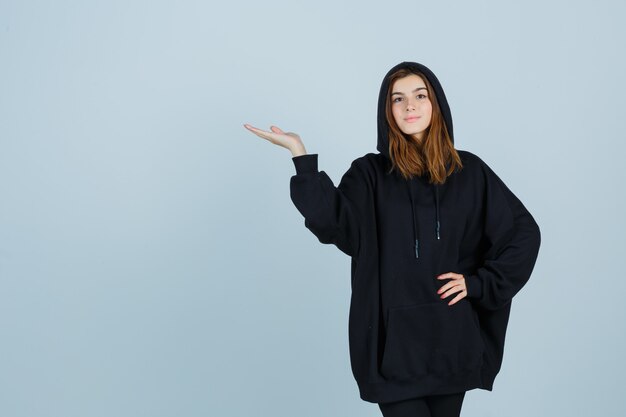 Young lady in oversized hoodie, pants pretending to hold something and looking confident , front view.