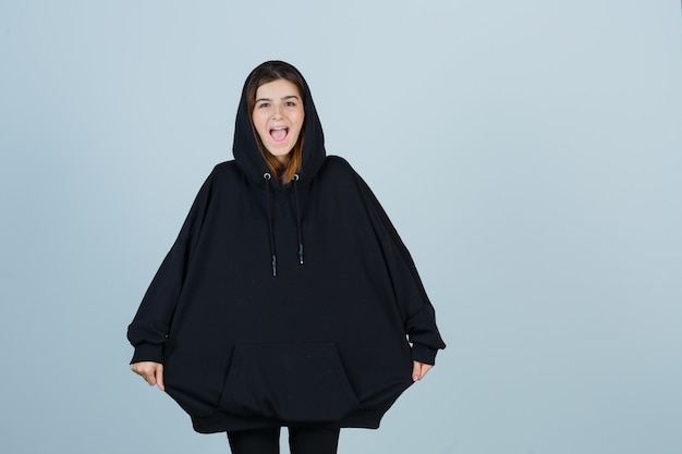 Free photo young lady in oversized hoodie, pants pulling hoodie with hands and looking funny , front view.