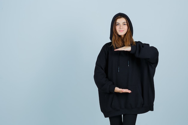 Foto gratuita giovane donna in felpa con cappuccio oversize, pantaloni che mostrano il segno di taglia e che sembra sicura di sé, vista frontale.