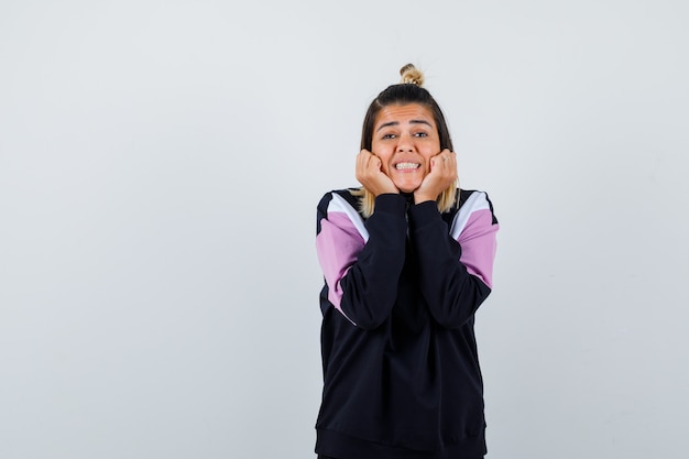 Young lady pillowing face on her hands in hoodie sweater and looking joyful