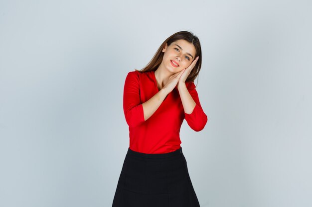 Young lady pillowing face on her hands in red blouse, skirt and looking sleepy