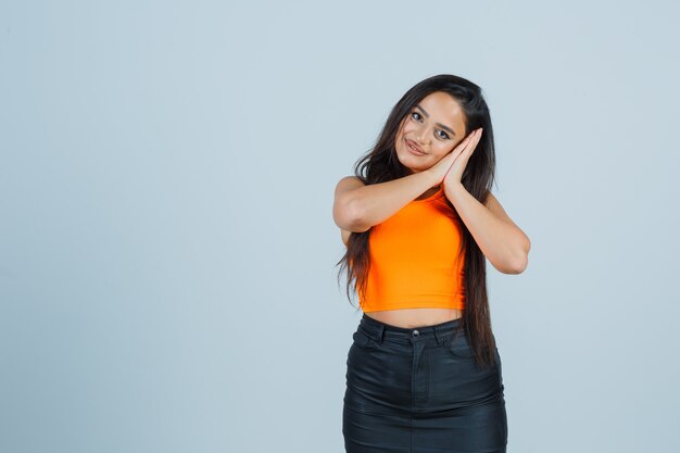 Young lady pillowing face on her hands in singlet, mini skirt and looking sleepy. front view.