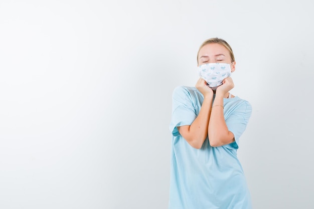 Young lady pillowing face on her hands in t-shirt, mask and looking peaceful