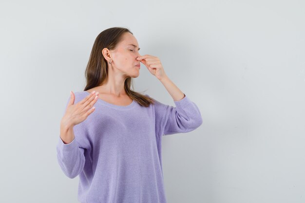 Young lady pinching nose due to bad smell in casual shirt and looking disgusted. front view.