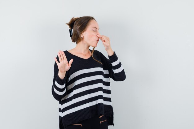 Young lady pinching nose due to bad smell in casual shirt and looking disgusted