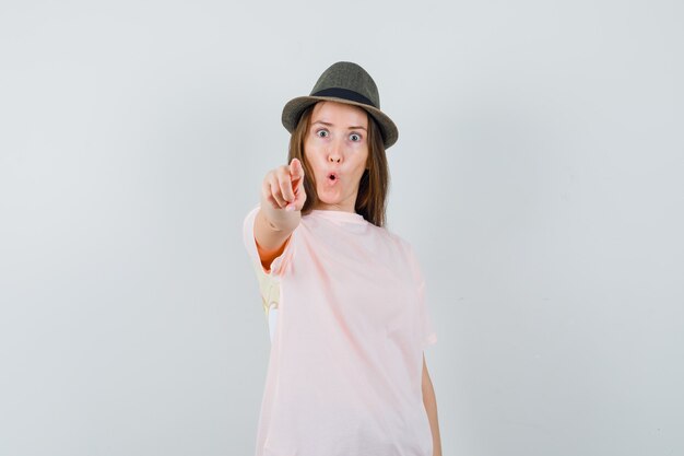Young lady in pink t-shirt hat pointing at camera and looking surprised