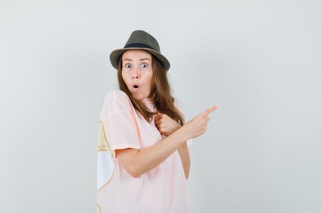 Young lady in pink t-shirt hat pointing to the right side and looking wondered