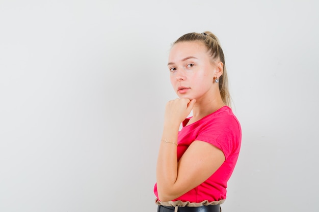 Young lady in pink t-shirt propping chin on raised fist and looking sensible 