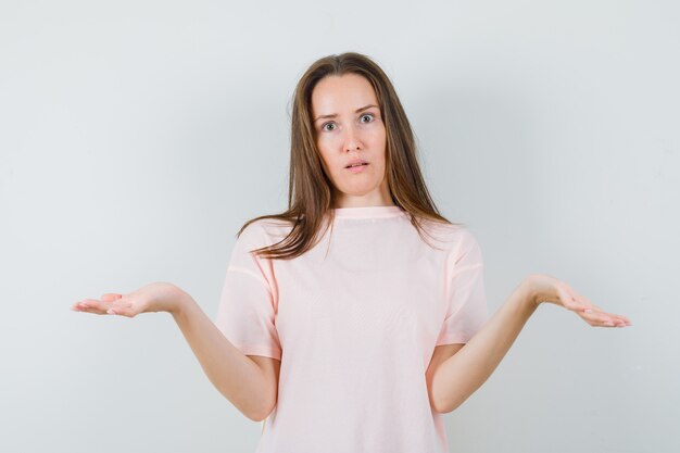 Young lady in pink t-shirt showing helpless gesture and looking confused , front view.