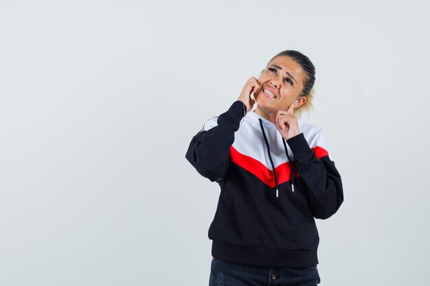 Young lady plugging ears while looking up in colorful sweatshirt and looking stressful. front view