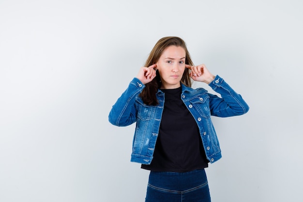 Young lady plugging ears with fingers in blouse and looking confident , front view.