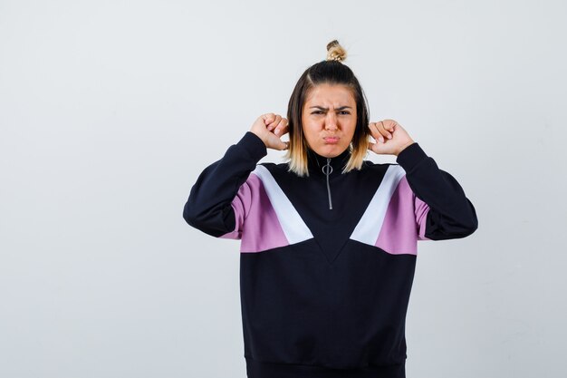 Young lady plugging ears with fingers in hoodie sweater and looking sorrowful