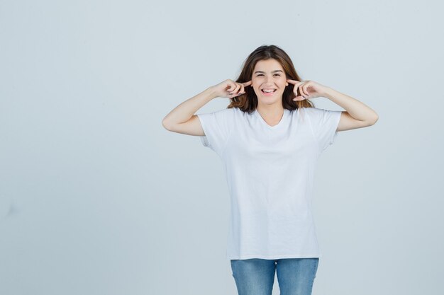 若い女性がTシャツ、ジーンズに指で耳を差し込んで、嬉しそうに見える、正面図。