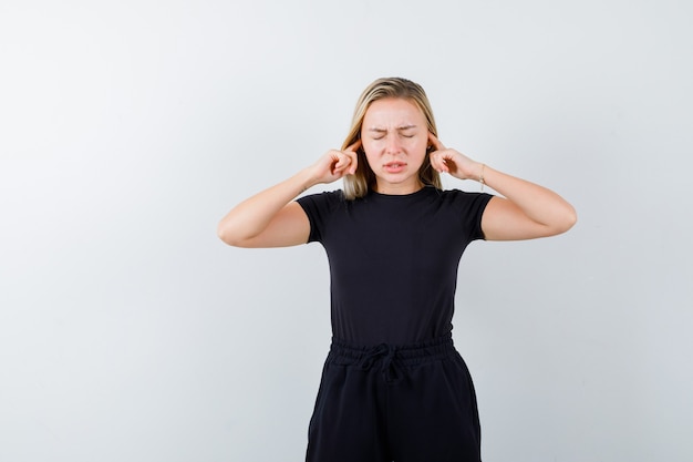 Foto gratuita giovane donna che collega le orecchie con le dita in maglietta, pantaloni e sembra angosciata vista frontale.