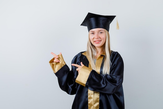 Young lady pointing aside in academic dress and looking blissful