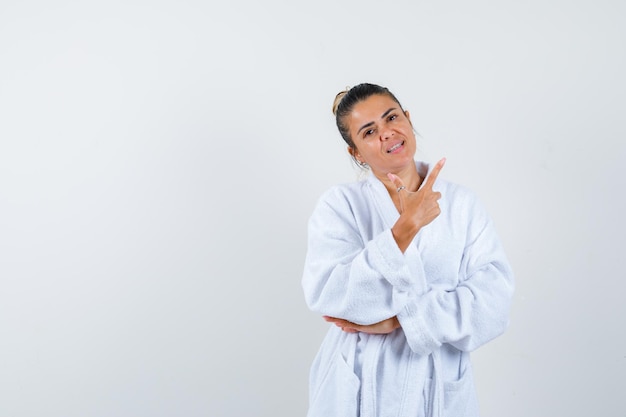 Young lady pointing aside in bathrobe and looking cheerful