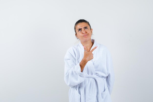 Young lady pointing aside in bathrobe and looking pensive
