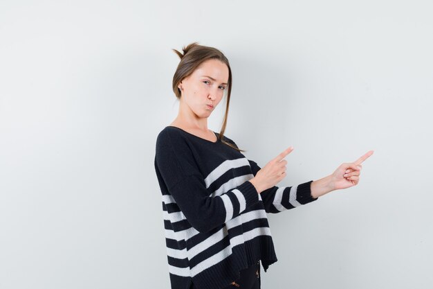 Young lady pointing aside in casual shirt and looking pensive