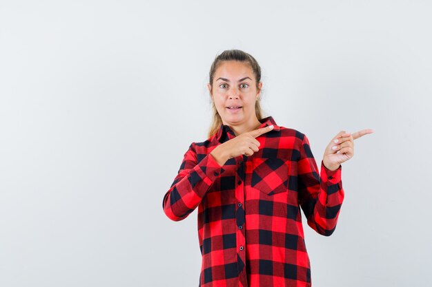 Young lady pointing aside in checked shirt and looking amazed