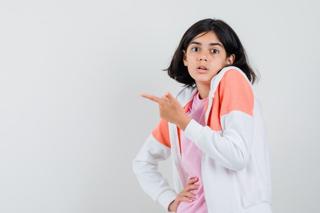 Young lady pointing aside in jacket, pink shirt and looking focused