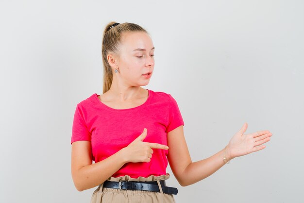 Young lady pointing aside, pretending to show something in pink t-shirt and pants and looking focused
