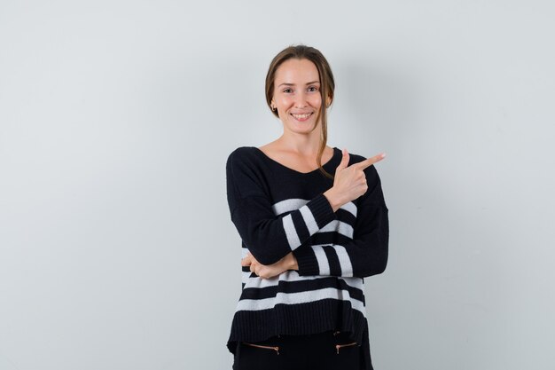 Young lady pointing aside in shirt and looking cheery