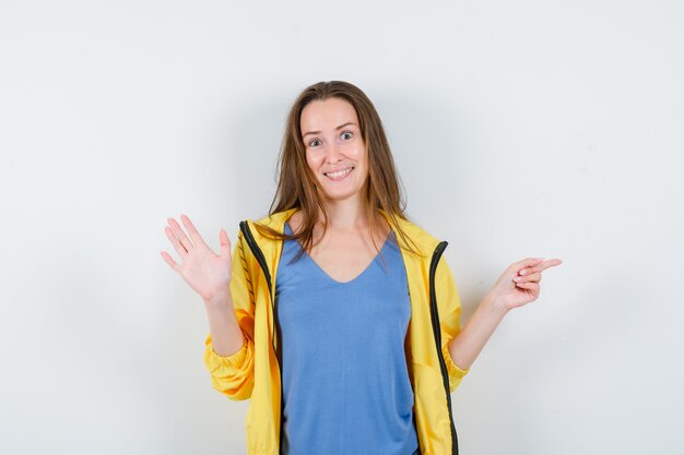 Young lady pointing aside, showing palm in t-shirt, jacket and looking happy. front view.