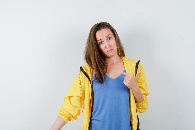 Young lady pointing aside in t-shirt and looking hesitant. front view.