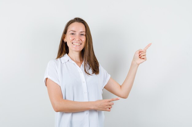 Young lady pointing aside while smiling in white blouse and looking satisfied