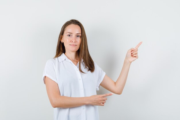 Young lady pointing aside in white blouse and looking calm