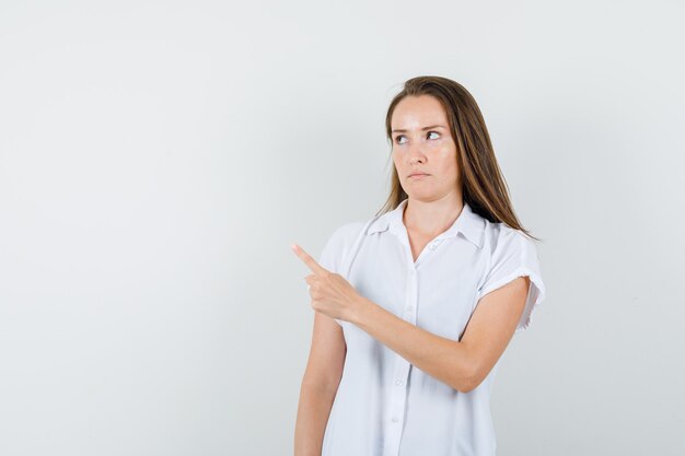 Young lady pointing aside in white blouse and looking dissatisfied