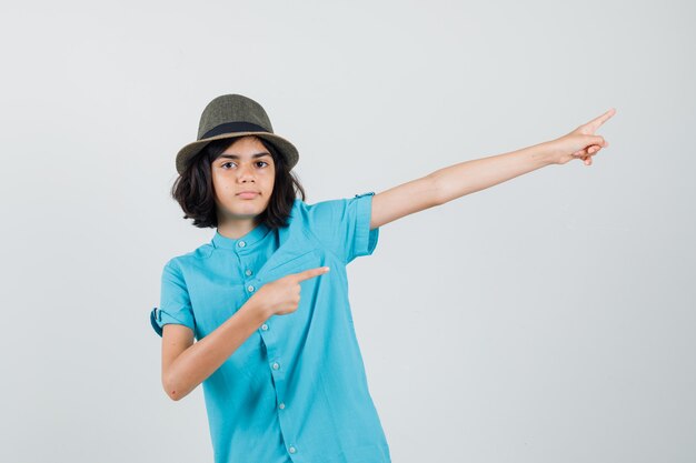 Young lady pointing away in blue shirt, hat and looking assured.