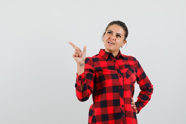 Young lady pointing away in checked shirt and looking dreamy