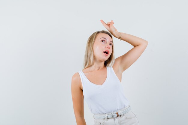 Young lady pointing away over head while talking in white blouse and looking pensive