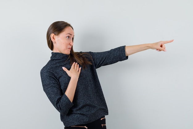 Free photo young lady pointing away in shirt and looking curious