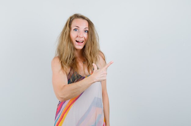 Young lady pointing away in summer dress and looking cheerful. 