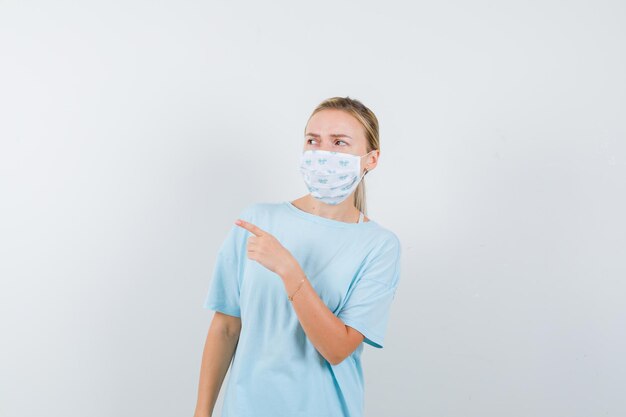 Young lady pointing away in t-shirt, mask and looking focused
