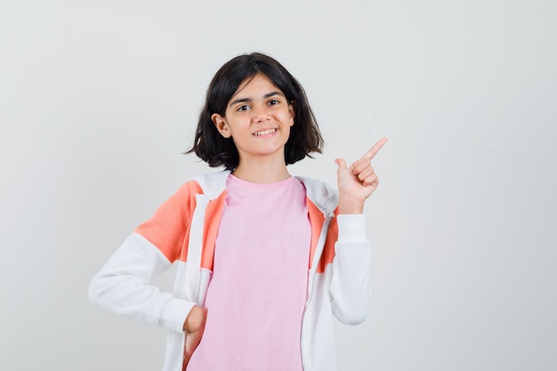 Young lady pointing away while smiling in jacket, pink shirt and looking merry.