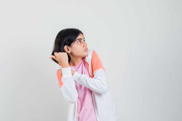 Young lady pointing back in jacket, pink shirt and looking scared.