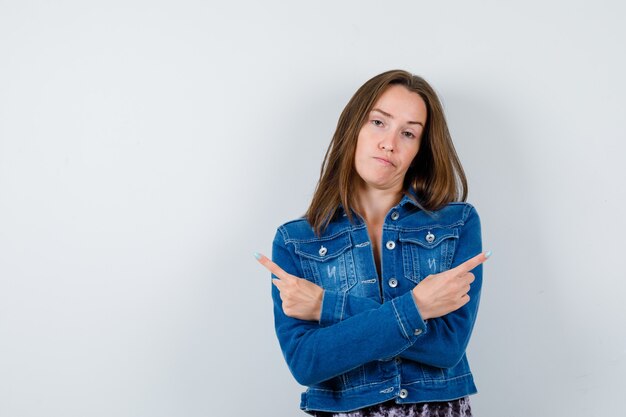 Young lady pointing to both sides in blouse, denim jacket and looking indecisive. front view.