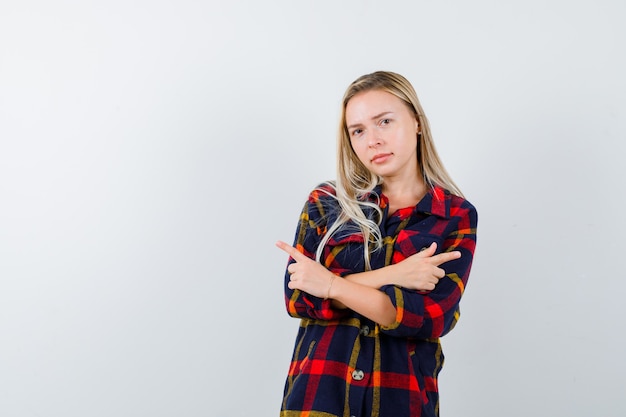 Young lady pointing at both sides in checked shirt and looking hesitant. front view.