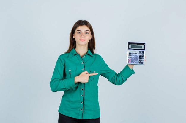 Young lady pointing at calculator in green shirt and looking confident. front view.