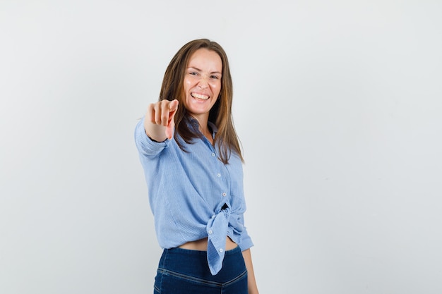 Young lady pointing at camera in blue shirt, pants and looking happy