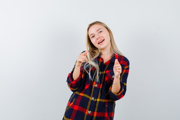 Young lady pointing at camera in checked shirt and looking energetic , front view.