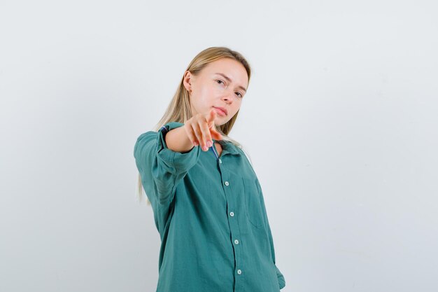 Young lady pointing at camera in green shirt and looking confident.