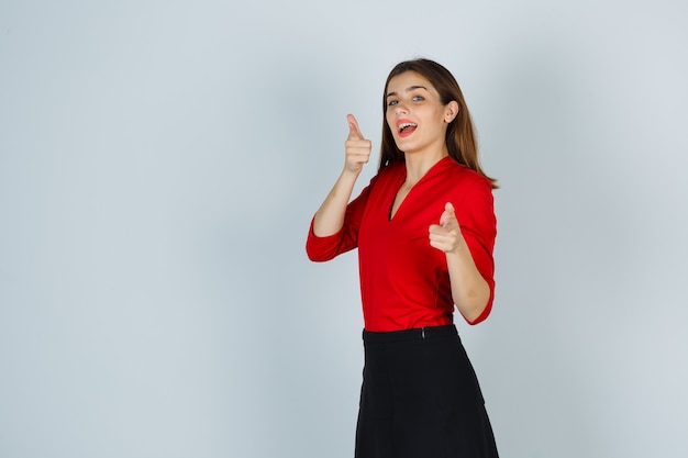 Young lady pointing at camera in red blouse, skirt and looking joyful