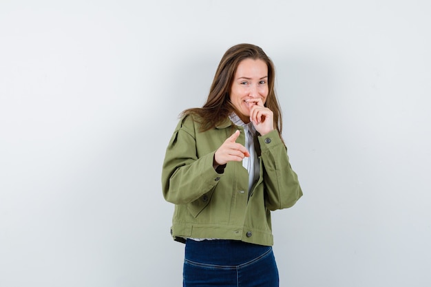 Young lady pointing at camera in shirt and looking happy. front view.