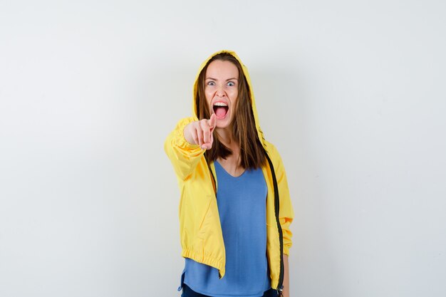 Young lady pointing at camera while screaming in t-shirt, jacket and looking angry. front view.