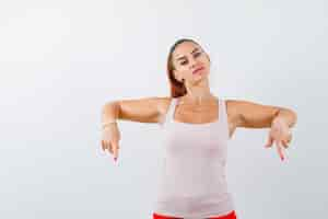 Free photo young lady pointing down in beige tank top and looking self-confident , front view.