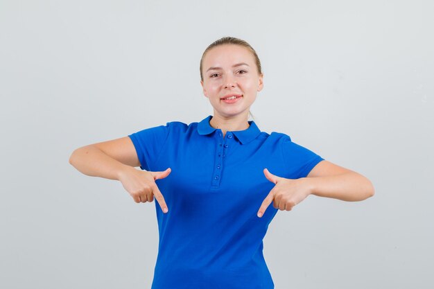 Young lady pointing down in blue t-shirt and looking merry